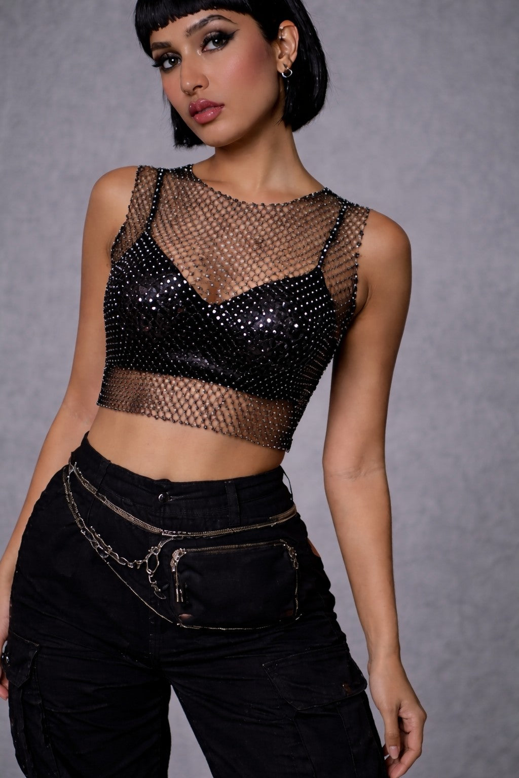 Close up of woman wearing FlexyDrip black rhinestone mesh top  and high-waisted black pants against a gray background