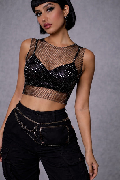 Close up of woman wearing FlexyDrip black rhinestone mesh top  and high-waisted black pants against a gray background