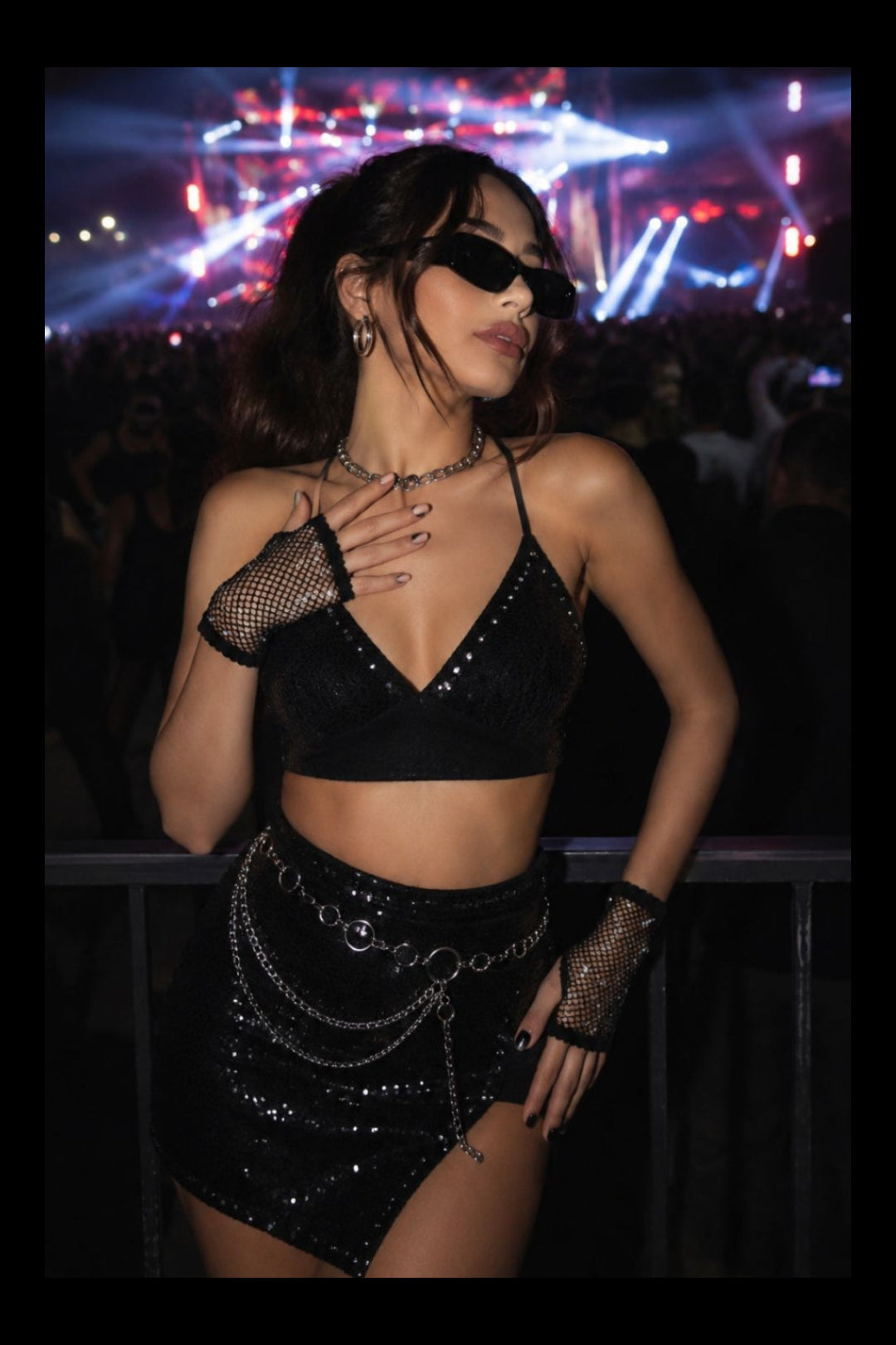 Woman in Flexydrip black fishnet pearl and rhinestone fishnet gloves, black sunglassesand black c0-ord set at a music concert.